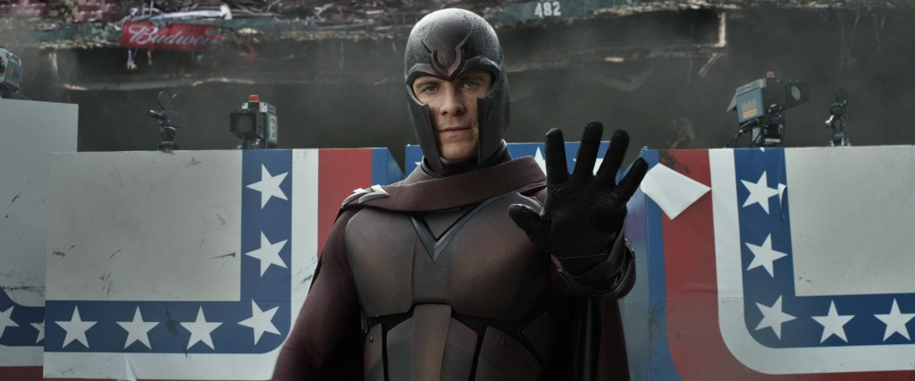 Magneto looks towards the camera with a raised hand, indicating he is using his power. The backdrop contains the remains of the RFK stadium and some stars-and-stripes theme banners.